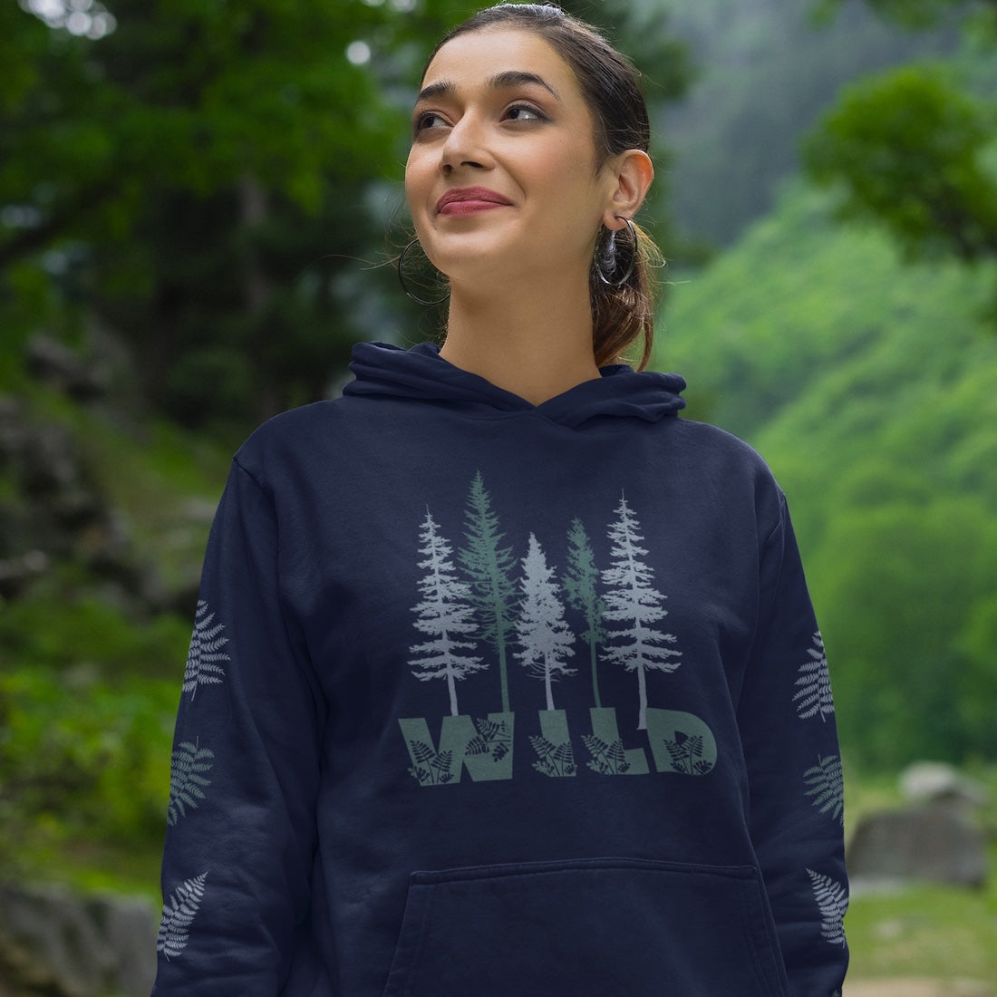 Woman wearing a navy nature hoodie with pine trees and says Wild